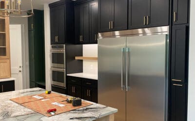 Modern home kitchen with black cabinet, marble countertop and brushed silver fridge